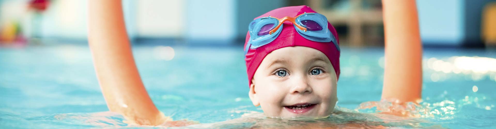 Child in pink swim cap with a swim noodle aid